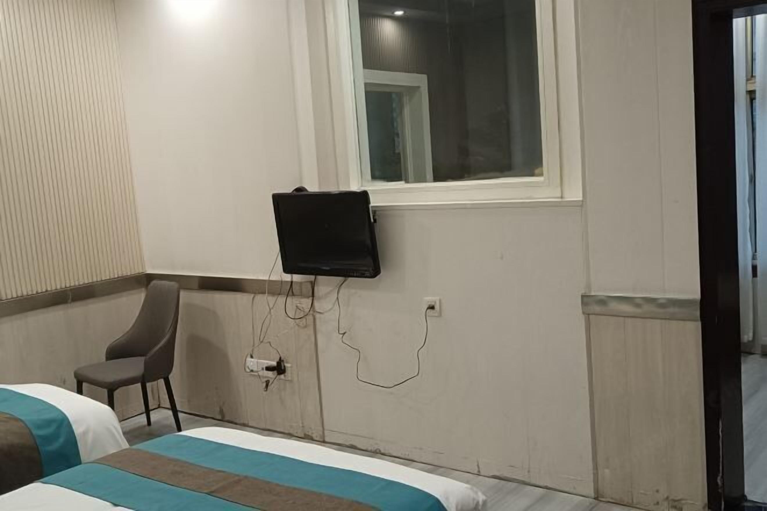 Ein Hotelzimmer mit einem Bett, einem Sessel, einem an der Wand montierten Fernseher und einem Fenster.