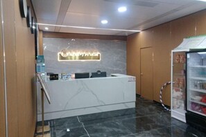 Un espace d’accueil comprenant un comptoir de réception en marbre, un luminaire fixé au mur et un distributeur automatique.
