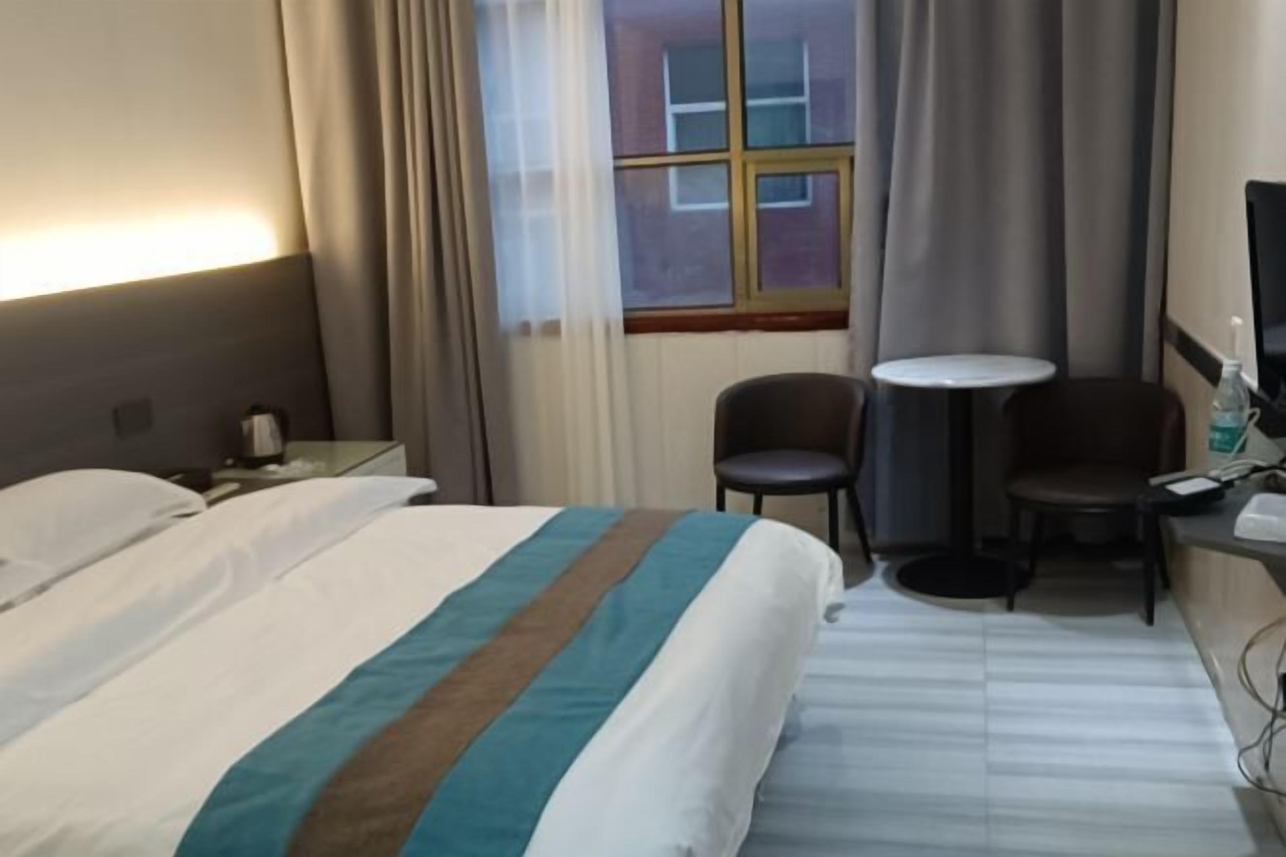 Een hotelkamer met een bed, een bureau, een stoel, een klein tafeltje en een raam met gordijnen.
