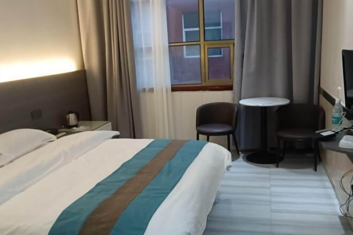 Une chambre d’hôtel avec un lit, un bureau, une chaise, une petite table et une fenêtre avec des rideaux.