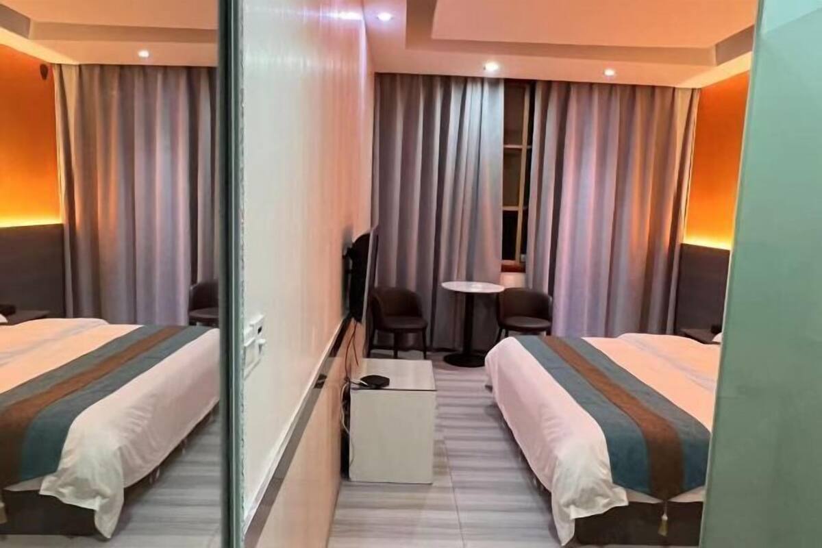 Habitación de hotel con dos camas, una mesita, sillas, televisor y ventana con cortinas.