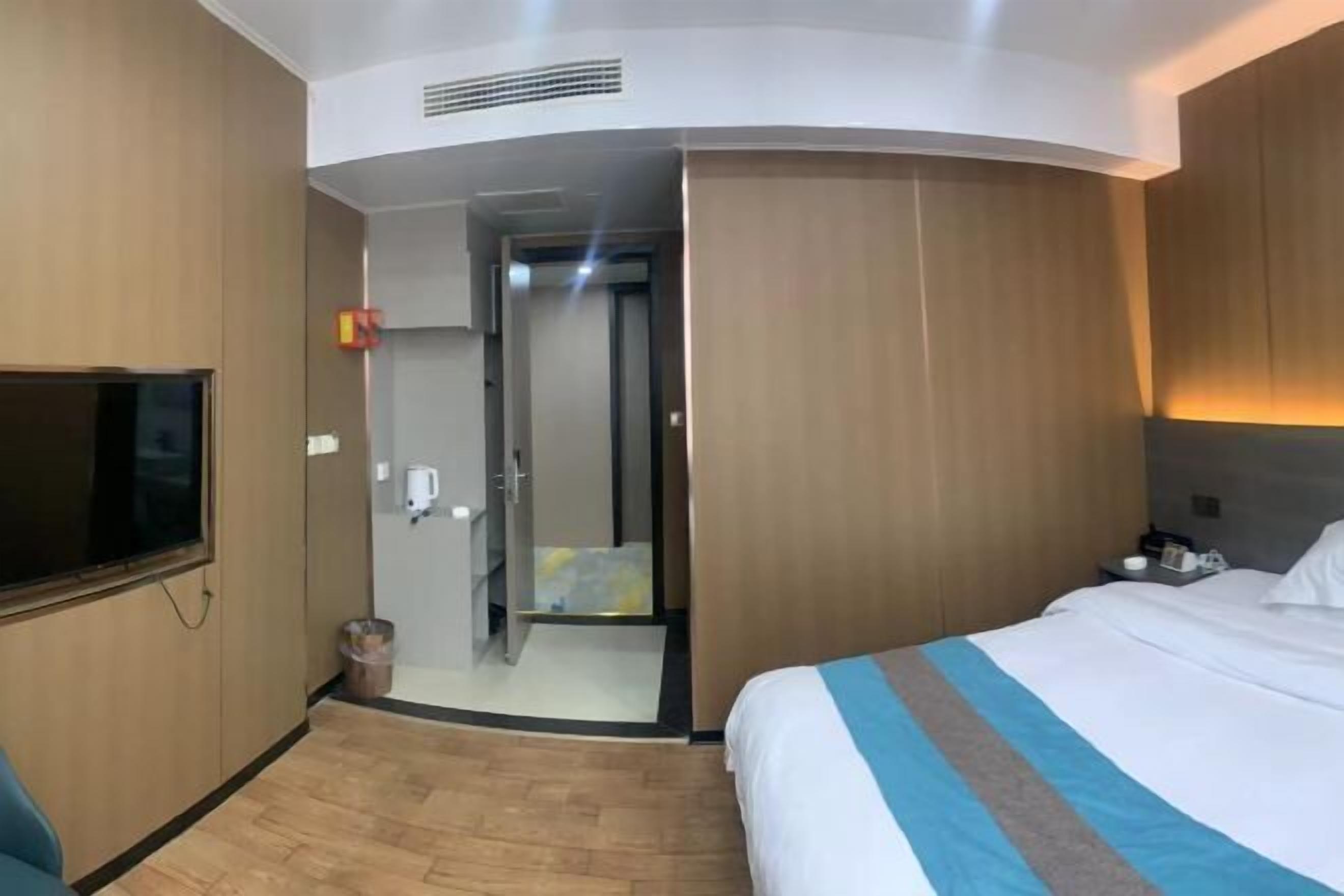 Una camera d'albergo con un letto, una televisione, uno specchio e un ingresso che dà su un bagno.