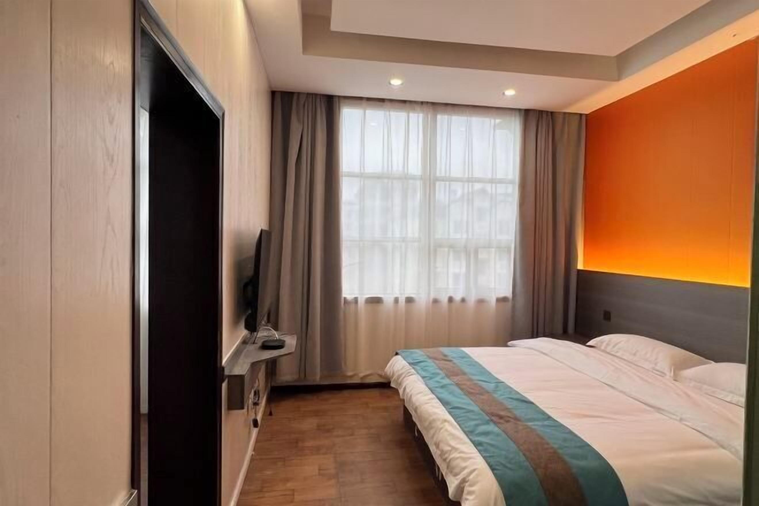 A hotel room with a bed, a TV, a desk, and a window with curtains.