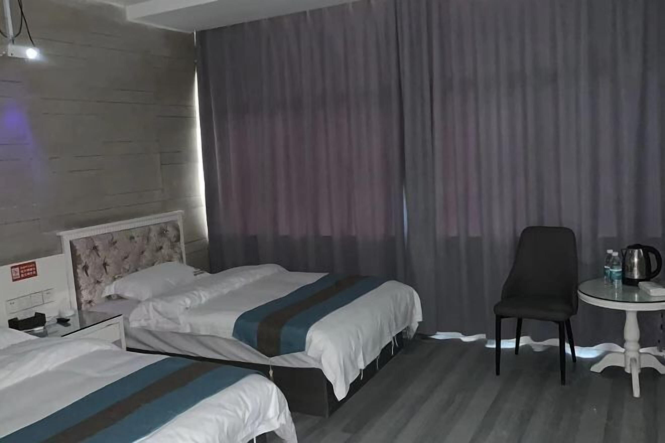A hotel room with two beds, a small table with a chair, and a curtain.