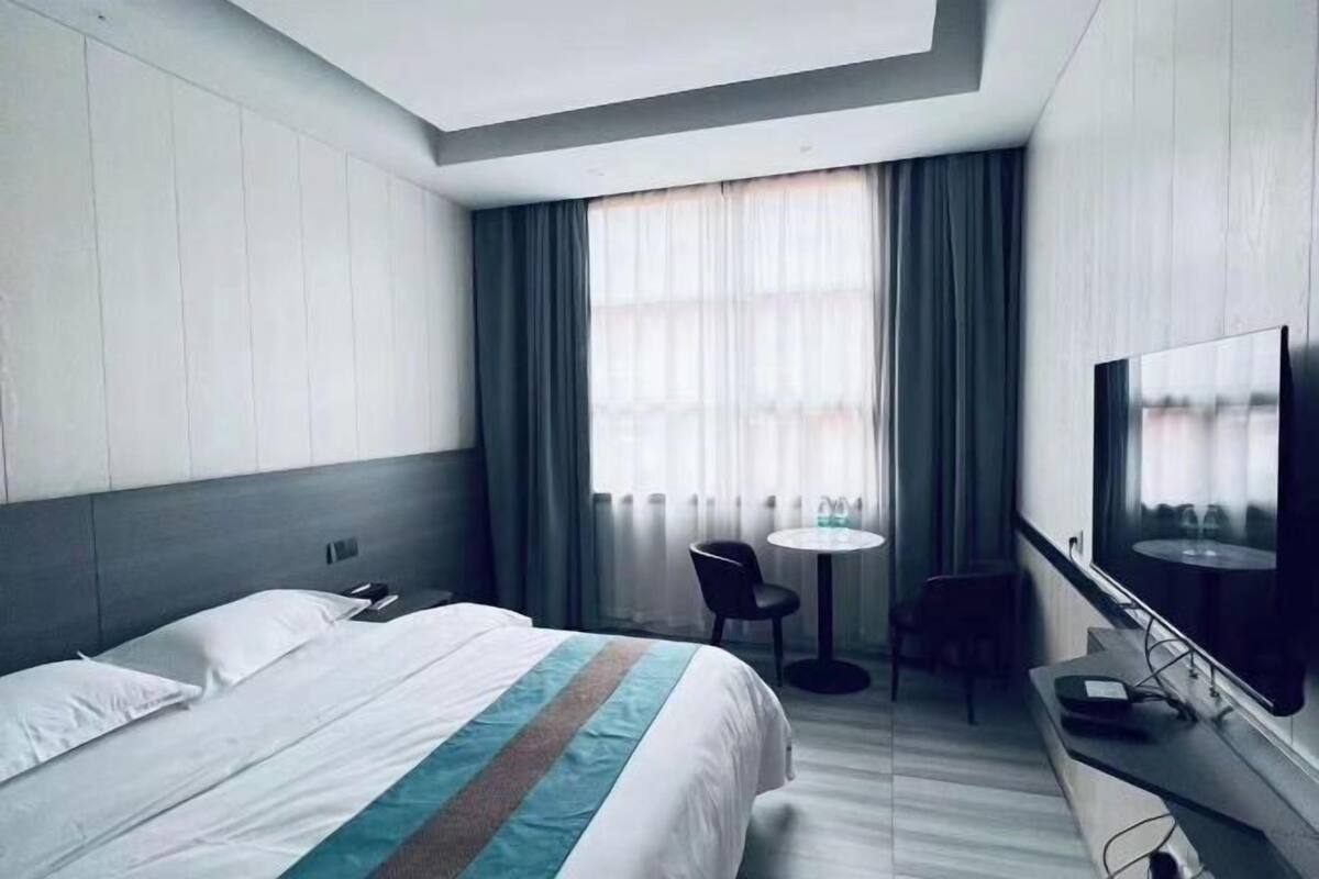 Habitación de hotel con cama, escritorio, silla, televisor y ventana con cortinas.