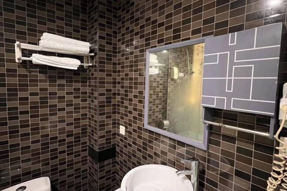 Un baño con paredes de azulejos oscuros, un lavamanos blanco y un perchero para toallas.