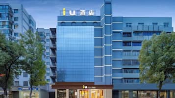 A hotel with a modern glass facade, a prominent 'i' logo, and a ground-level entrance with illuminated signage.
