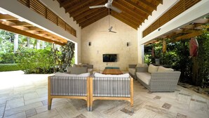 Un vaste patio doté d’un plafond en bois, d’un téléviseur à écran plat fixé au mur et d’un espace détente composé d’un canapé et d’une chaise longue.