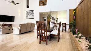 Un salon spacieux doté d’un grand téléviseur à écran plat, d’un canapé beige et d’un coin repas avec des chaises en bois et une table en verre.