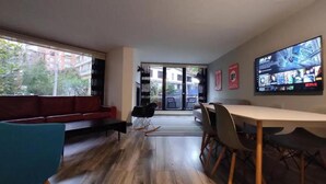 A modern interior with a red sofa, a dining table with chairs, a TV displaying Netflix content, and a view of the outside through a glass door. - Apartamentos El Árbol (Bogotá)