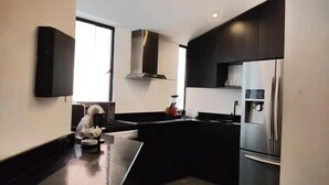 A modern kitchen with a central island, black cabinetry, stainless steel appliances, and a large window providing natural light. - Apartamentos El Árbol (Bogotá)
