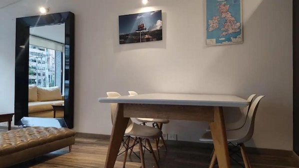 A modern room with a large mirror, a dining table with chairs, a sofa, and wall art including a map and a landscape painting.