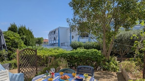An outdoor dining area with a table set for two, surrounded by greenery and a building in the background. - Sol-y-Days Floralies 2, Studio with terrace and swimming pool (Le Grau-du-Roi)
