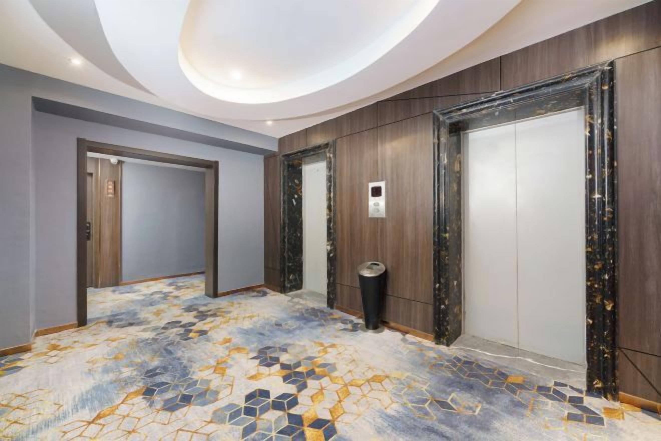 A hotel corridor with a patterned floor, wooden panel walls, and a ceiling with recessed lighting.