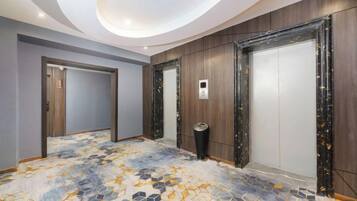 A hotel corridor with a patterned floor, wooden panel walls, and a ceiling with recessed lighting.
