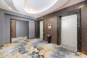 A hotel corridor with a patterned floor, wooden panel walls, and a ceiling with recessed lighting. - Korla Ronghui Yi Hotel (Xiangli Avenue Food Street Branch) (Korla)