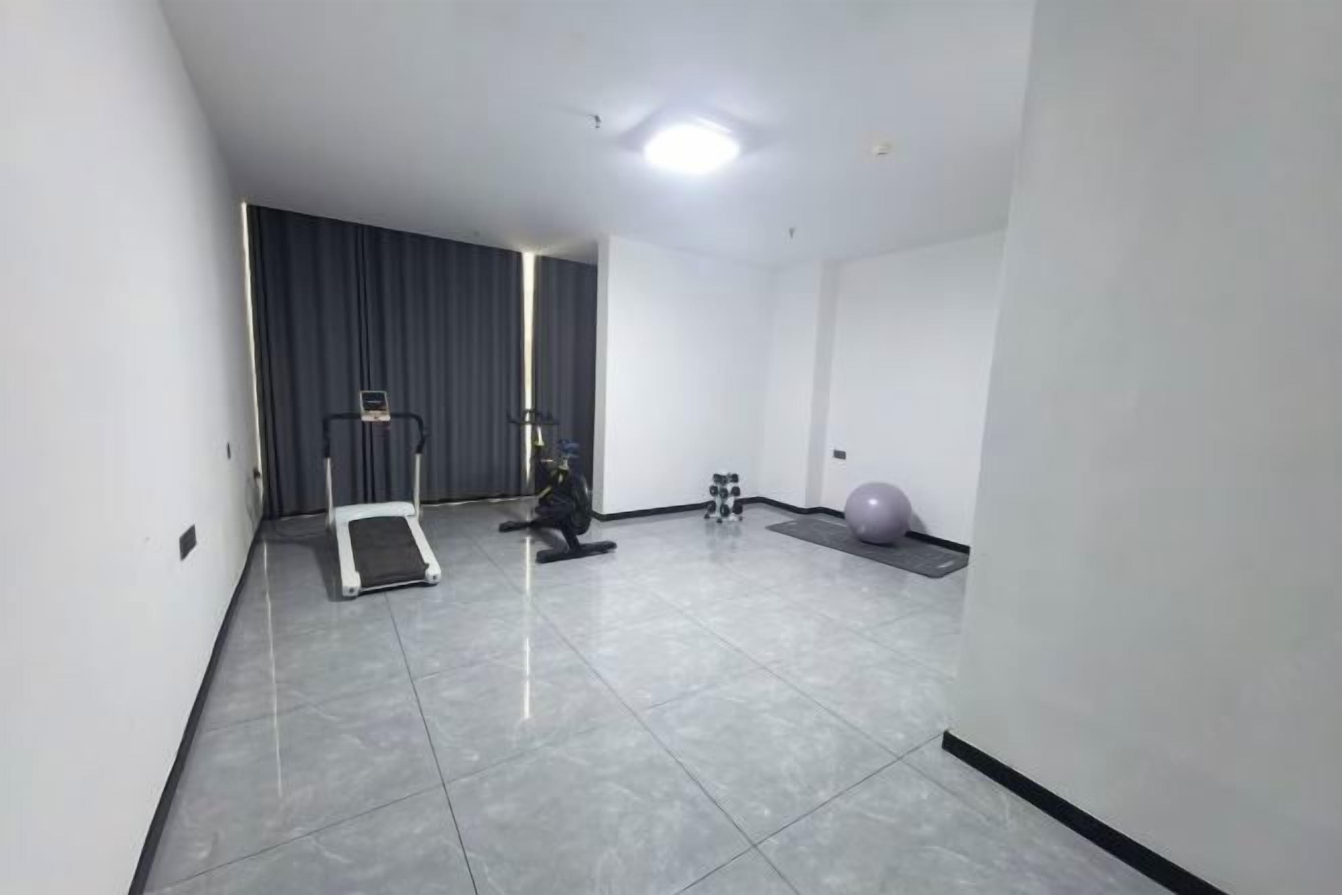 A room with a treadmill, exercise ball, and weights.