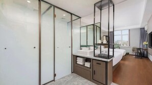 A modern hotel room with a glass partition, a large bed, a bathroom with a sink and mirror, and a city view. - Korla Ronghui Yi Hotel (Xiangli Avenue Food Street Branch) (Korla)
