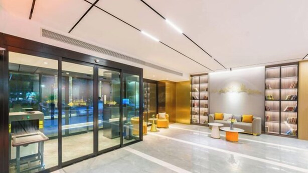 A modern lobby with a glass partition, seating area with sofas and tables, and a bookshelf. - Korla Ronghui Yi Hotel (Xiangli Avenue Food Street Branch) (Korla)