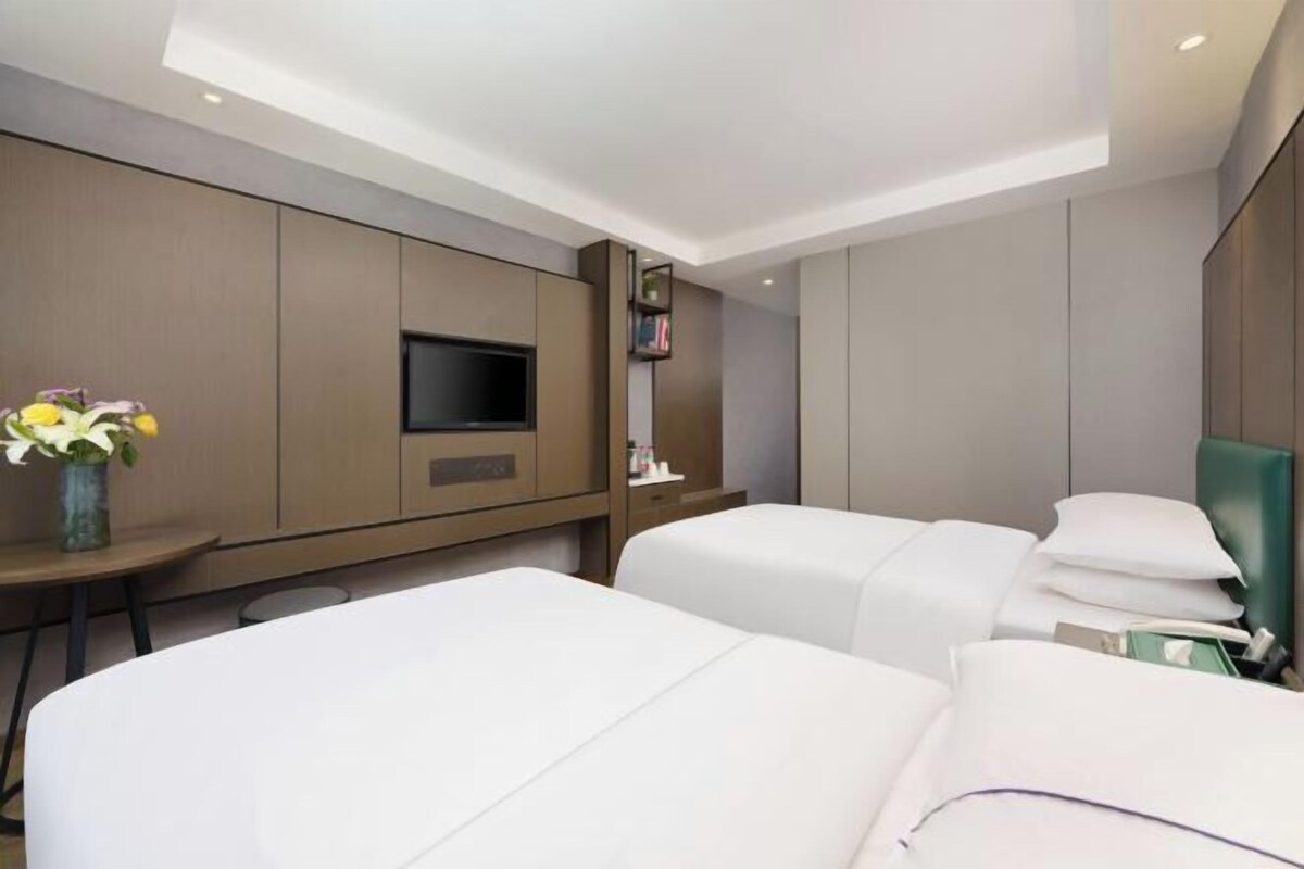 Une chambre d’hôtel moderne équipée de deux lits, d’un téléviseur à écran plat, d’une petite table et d’une bibliothèque.