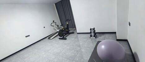 A room with a grey exercise bike, a stationary bike, and a large purple exercise ball.