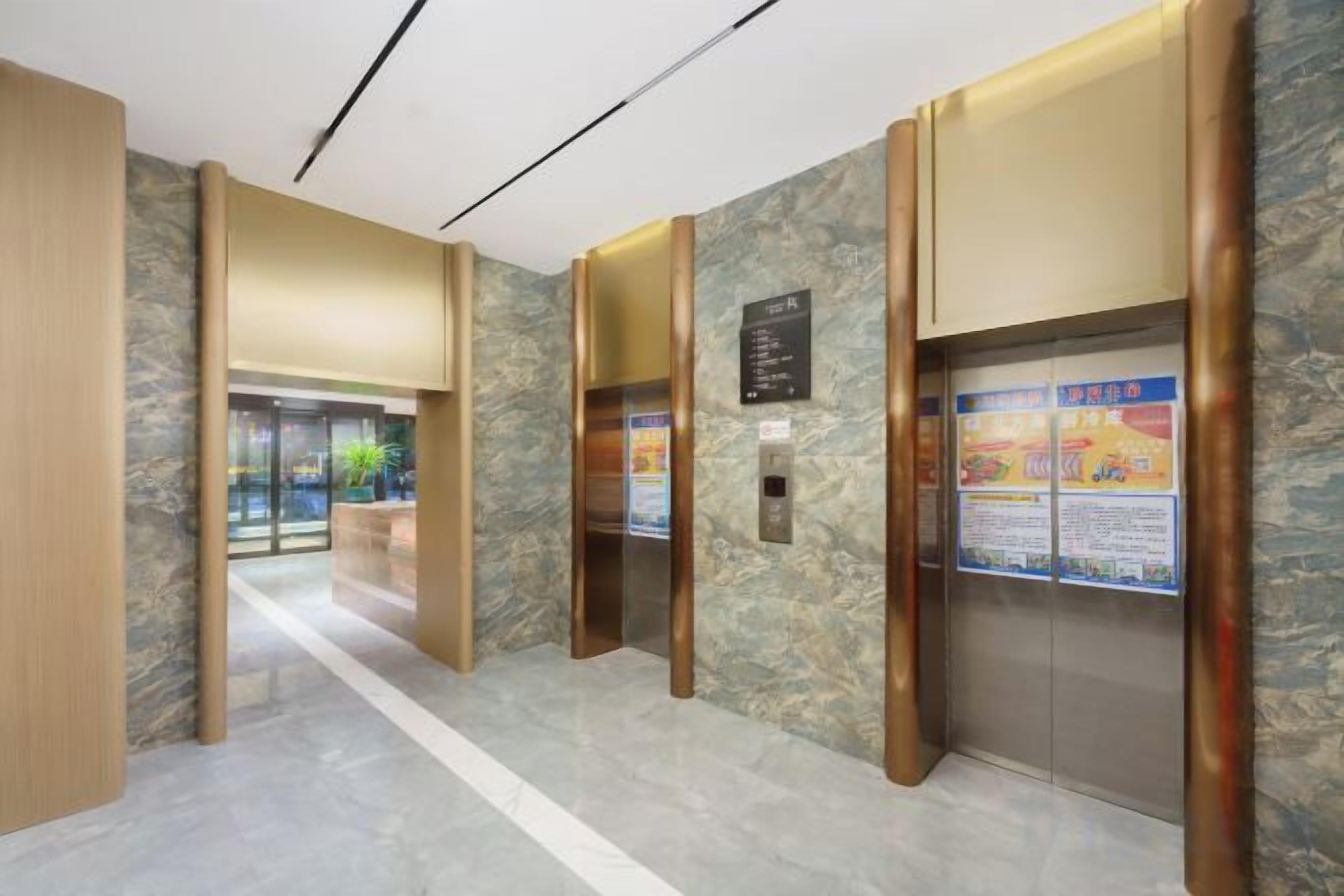 A hotel lobby with marble flooring, wooden accents, and an elevator with informational posters.