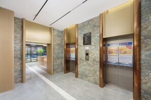 A hotel lobby with marble flooring, wooden accents, and an elevator with informational posters. - Korla Ronghui Yi Hotel (Xiangli Avenue Food Street Branch) (Korla)