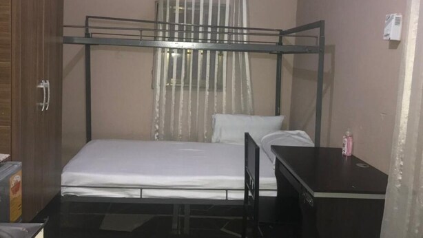 A single bed with a metal frame, a bedside table, a curtain, and a wardrobe.