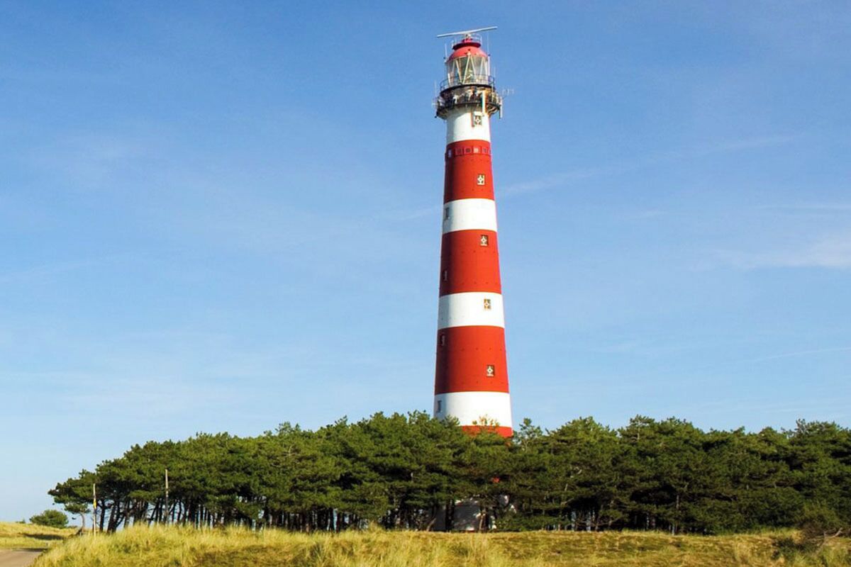 Un grand phare aux bandes rouges et blanches alternées, entouré d’arbres.