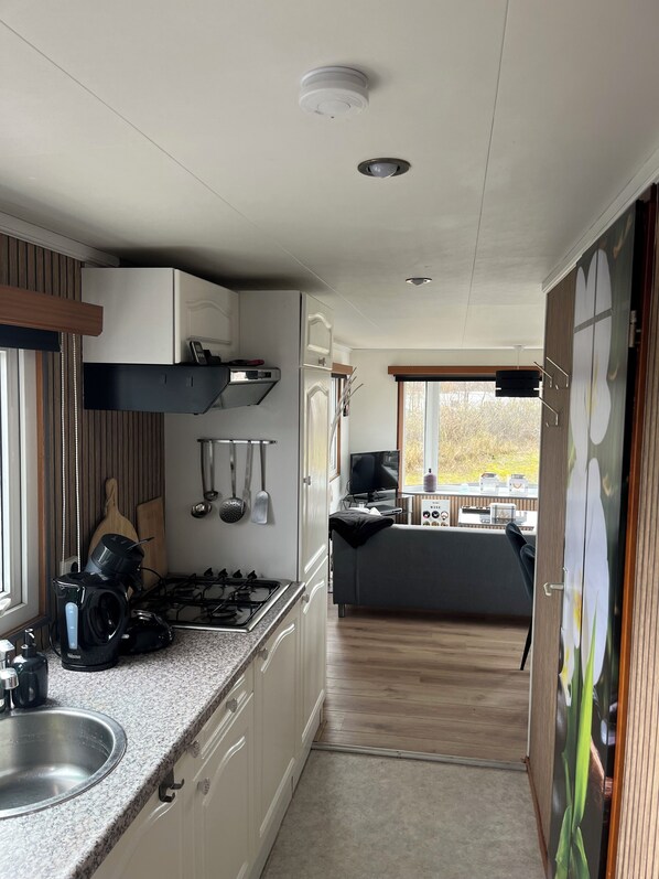 A compact kitchen with a gas stove, a sink, and a microwave. There is a window providing natural light and a view of the outdoors.