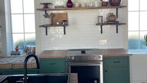 A kitchen with a stove, sink, and green cabinets. There are two windows with arched tops, a shelf with kitchen items, and a framed picture on the wall. - St. Chris - Graham, TX (Graham)