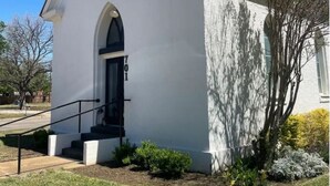 A white building with a black door and a small set of stairs leading up to the entrance. - St. Chris - Graham, TX (Graham)