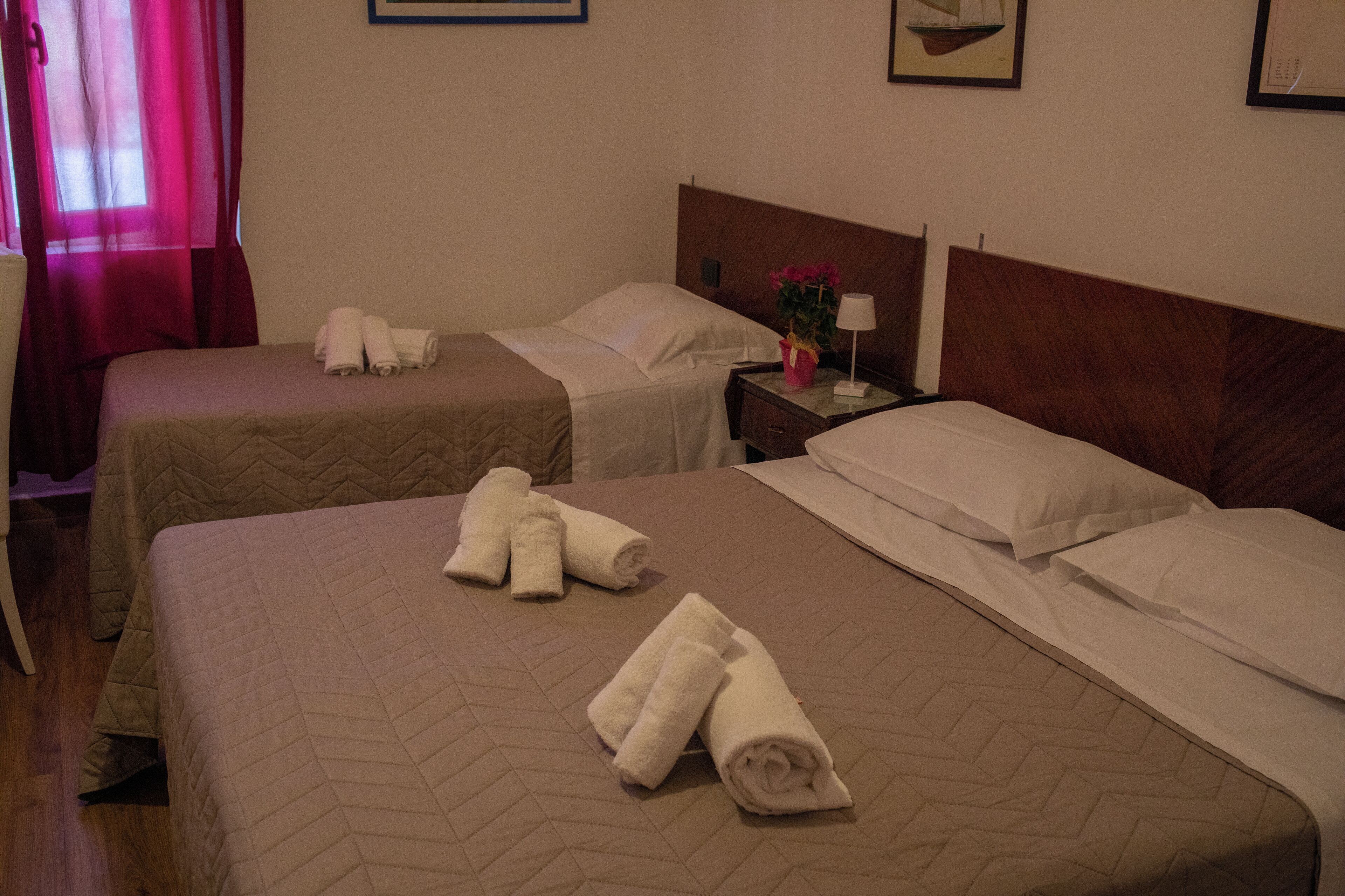 Habitación de hotel con dos camas, cada una con toallas ordenadas y un cabecero de madera.