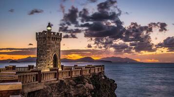 A stone tower with a lantern on top, overlooking a body of water with mountains in the background.