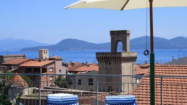 A coastal town with a prominent tower, terracotta-roofed buildings, and a clear view of the sea. - HOTEL ARISTON (Piombino)