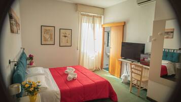 Habitación de hotel con cama, escritorio con computadora, televisión y baño visible a través de una puerta abierta.