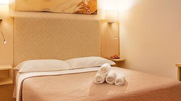 A neatly made bed with a quilted cover and three rolled towels on the side.