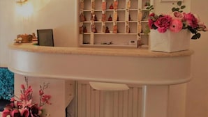 A reception area with a white counter, a wall-mounted shelf with numbered tags, a framed certificate, and a vase with pink flowers. - HOTEL ARISTON (Piombino)