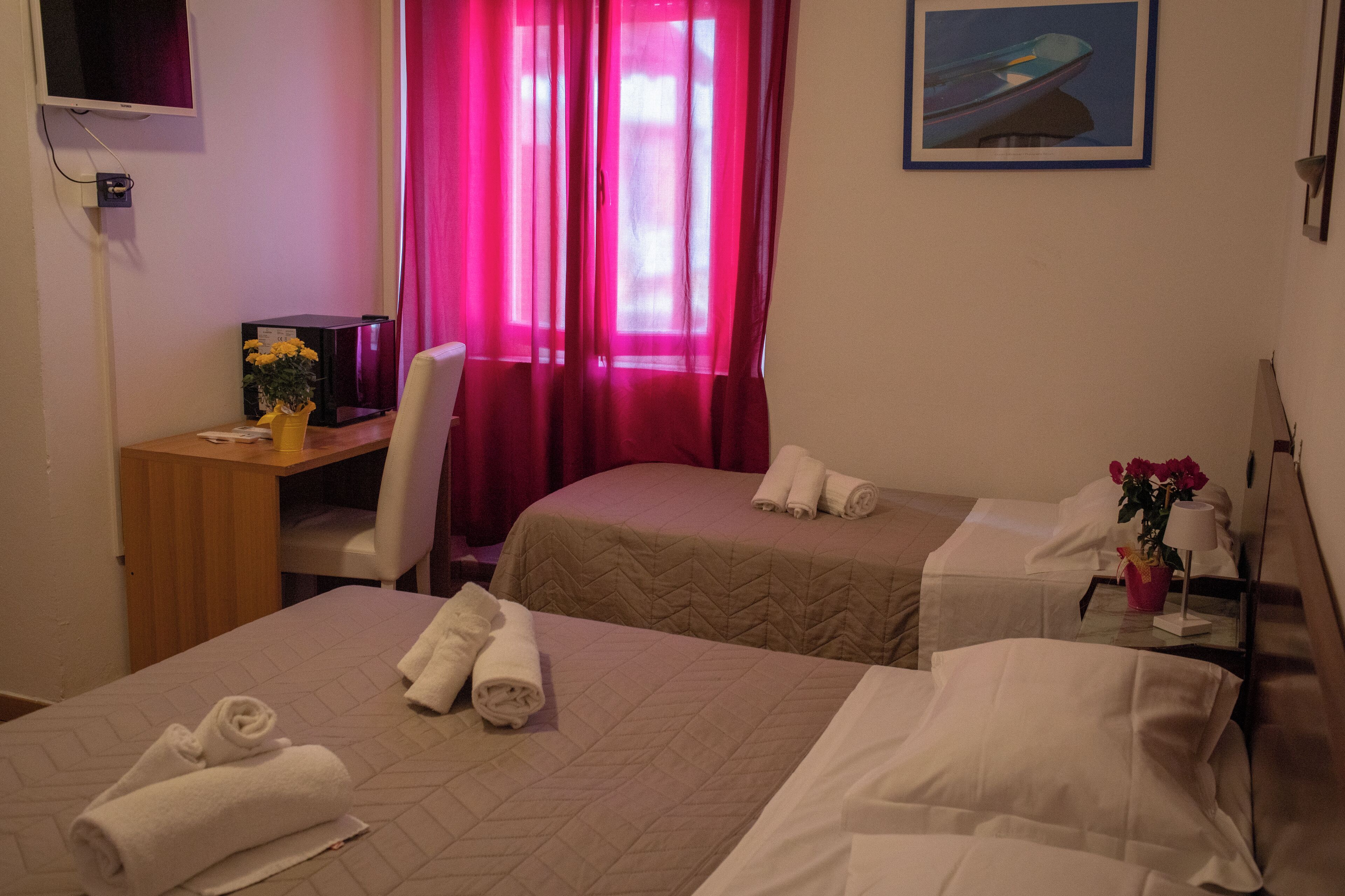 A hotel room with two beds, a desk, a chair, a TV, and a window with curtains.