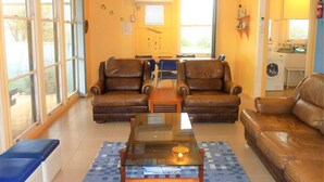A living room with two leather armchairs, a glass coffee table, and a sofa. There is a dining table with chairs in the background. - Gunnadoo, Moonta Bay (Moonta Bay)