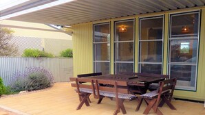 An outdoor patio with a wooden table and chairs, a covered area with windows, and a garden with plants. - Gunnadoo, Moonta Bay (Moonta Bay)