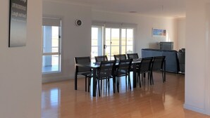 A spacious dining area with a table and chairs, a clock on the wall, and a view through the door.