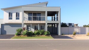 A modern two-story house with a garage, a balcony, and a well-maintained front yard with plants.