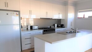 A modern kitchen with white cabinetry, a built-in island with a sink, a stove, and a toaster.