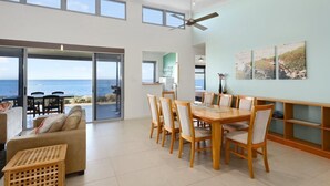 En rummelig opholdsstue med et stort spisebord, behagelige siddepladser og havudsigt gennem store skydedøre.
