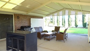 Ein überdachter Patio-Bereich mit Grill, Korbmöbeln und einer Ziegelwand.