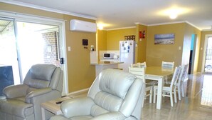 Ein Wohnzimmer mit einer Couch, einem Esstisch mit Stühlen, einer Küchenzeile mit Geräten und einer Glasschiebetür, die auf einen Balkon führt.