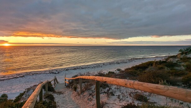 A wooden staircase leading down to a beach with a sunset in the background.
