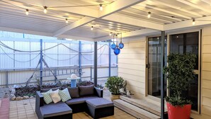 A covered patio with a cushioned seating area, potted plants, and hanging blue globes.