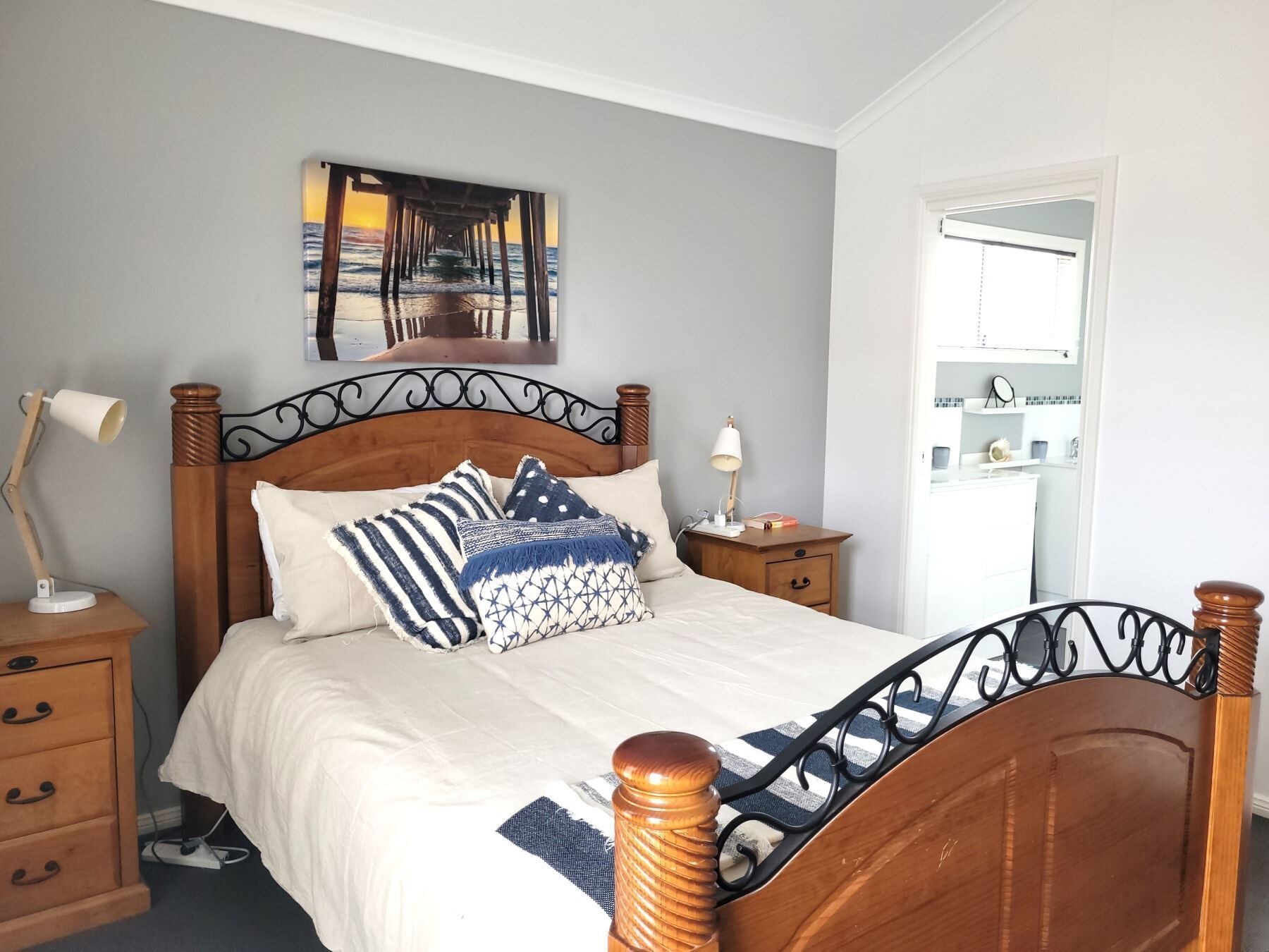 A neatly arranged bedroom with a wooden bed, a bedside table with a lamp, and a wall-mounted artwork.